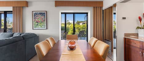 Un comedor moderno con una mesa de madera, sillas color beige y vistas a zonas verdes a través de grandes ventanales.