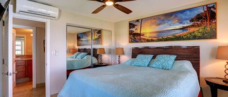 A hotel room with a bed, a ceiling fan, a painting, a mirror, and a view of the beach.