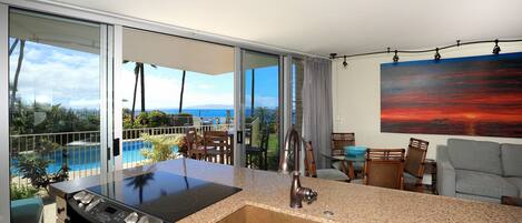 A modern kitchen with a large island, a stainless steel stove, and a view of a pool and ocean.