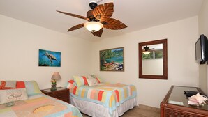 A bedroom with two beds, a ceiling fan, artwork on the walls, and a television on a stand. - Kamaole Nalu, #105 2 Bedroom Condo by RedAwning (Kihei)