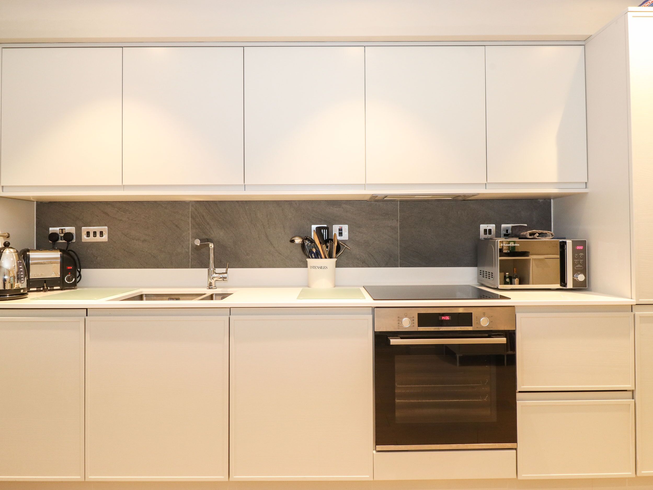 A modern kitchen with white cabinets, a stainless steel sink, a built-in oven, and a microwave.