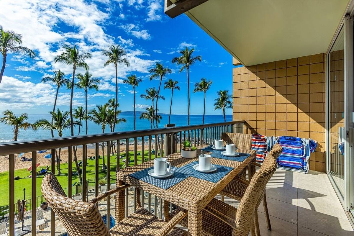 A balcony with wicker furniture, a table with cups, and a view of the beach and ocean.