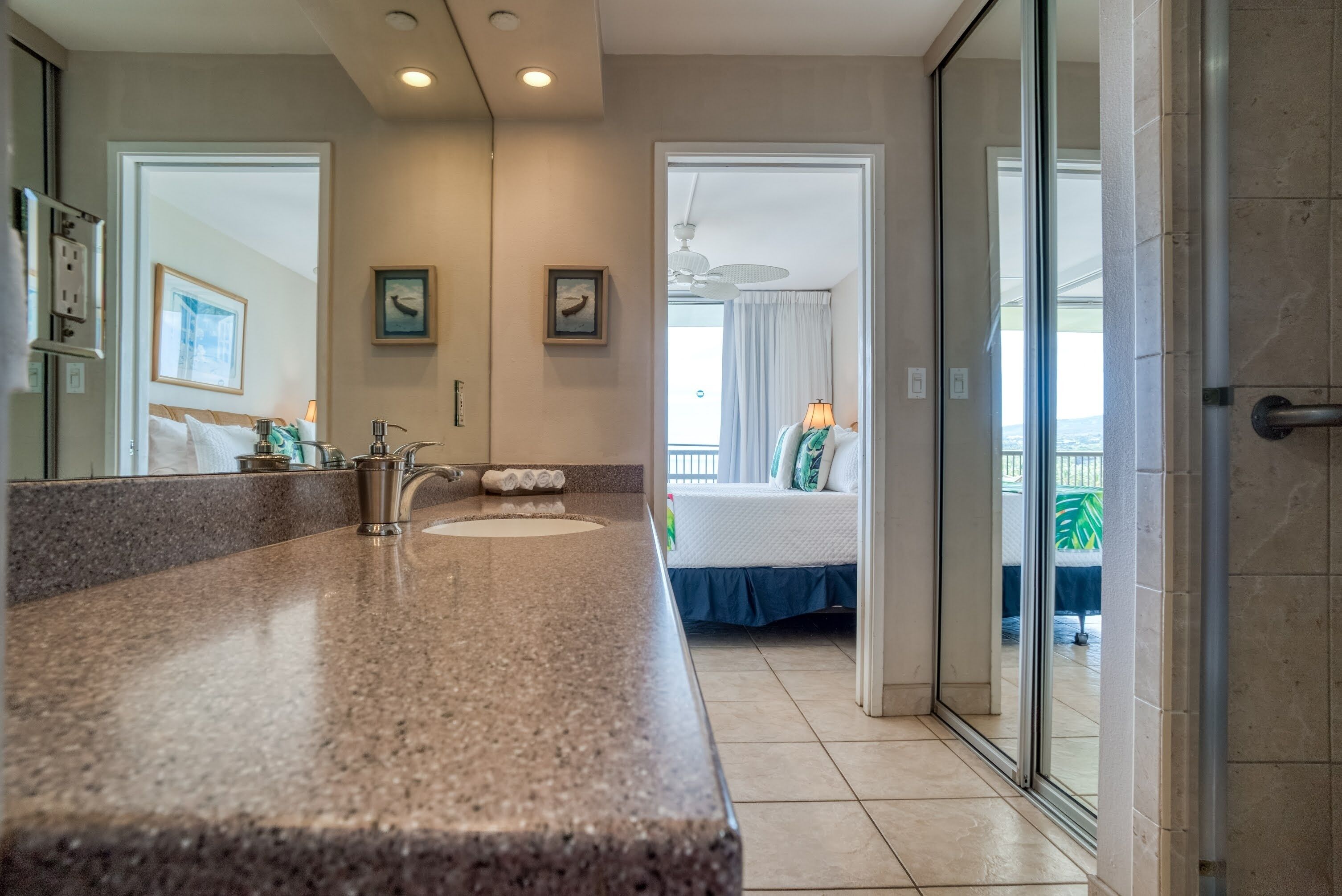 A bathroom with a granite countertop, two sinks, and a shower area.