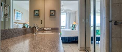 A bathroom with a granite countertop, two sinks, and a shower area.