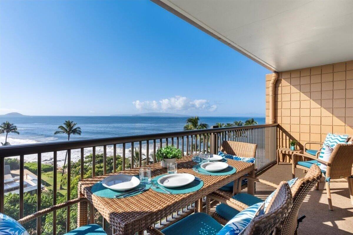 A balcony with wicker furniture, a table set for dining, and a view of the ocean.