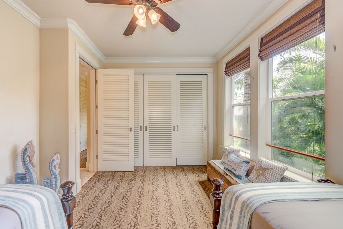 Une chambre à coucher avec un lit, une fenêtre donnant sur des palmiers, un ventilateur de plafond et un tapis à motifs.