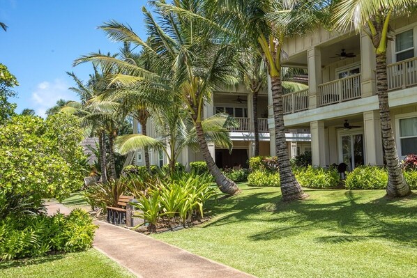 A multi-story hotel with a lush garden, palm trees, and a pathway leading to the entrance.