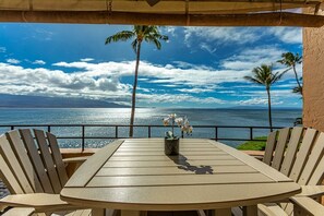 Ein runder Tisch mit Stühlen, einem Blumentopf und Blick auf das Meer mit Palmen.