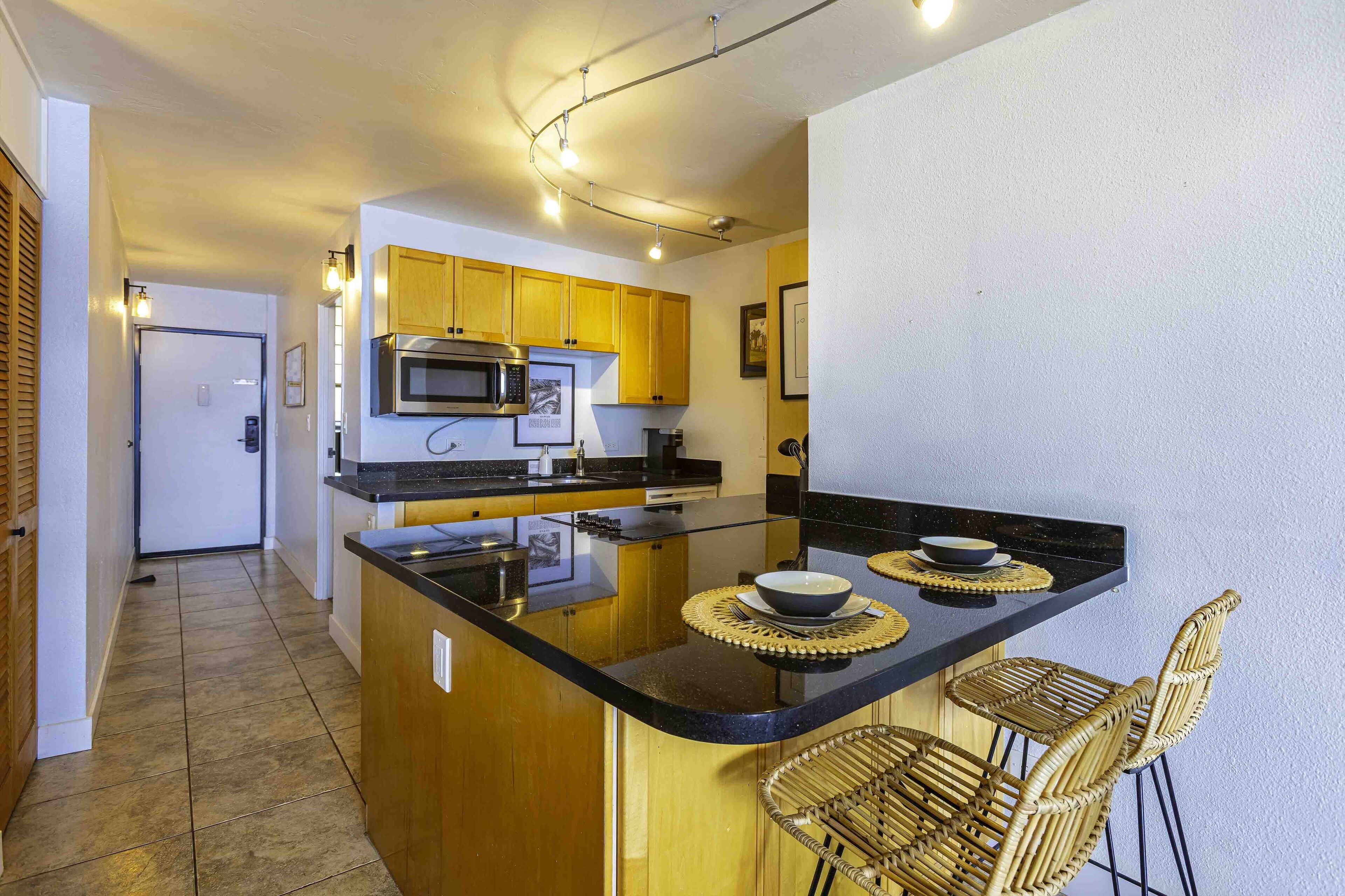 A modern kitchen with wooden cabinets, a black countertop, and a central island with bar stools.
