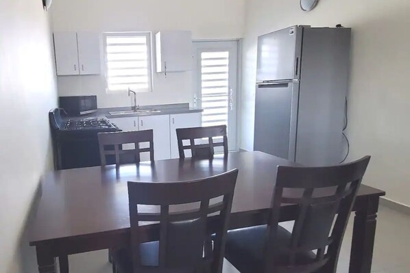 A compact kitchen with a refrigerator, stove, and microwave. There are two wooden chairs at a small dining table.