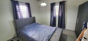 A bedroom with a bed, curtains, a wardrobe, and a hanging light fixture.