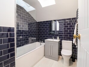 Een badkamer met bad, toilet en wastafel, met zwart-wit betegeling en een dakraam.