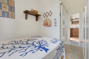 Un dormitorio con cama, repisa con cesta, un adorno de pared y vista a la cocina.
