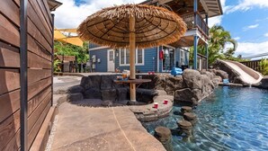 A pool area with a thatched umbrella, a slide, and a wooden deck. - The Cove Hale 4 Bedroom Home (Kihei)