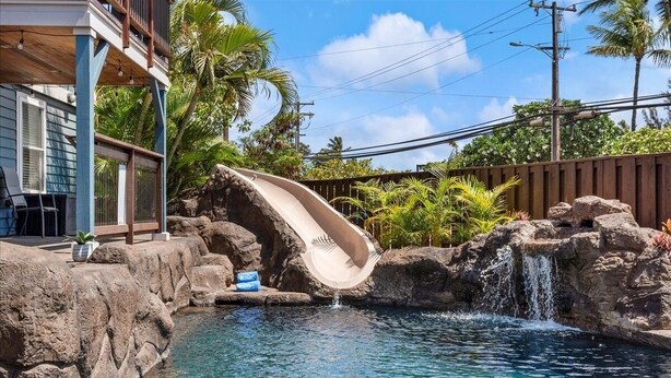 A pool with a water slide, surrounded by rocks and palm trees. - The Cove Hale 4 Bedroom Home (Kihei)