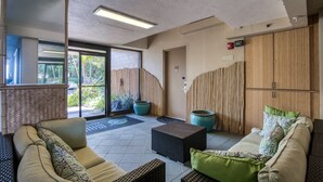 Un espace intérieur moderne comprenant un canapé, une petite table et un meuble. On y trouve une porte portant l’inscription « 101 » et une fenêtre donnant sur un paysage verdoyant.