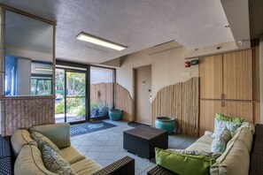 Un espacio interior moderno con un sofá, una mesita y un mueble. Hay una puerta con el letrero '101' y una ventana que ofrece vistas al follaje exterior.