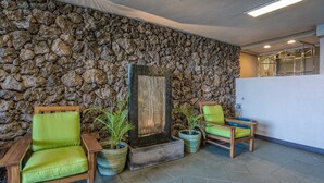 Un hall d’entrée aux murs en pierre, un comptoir d’accueil en bois et deux fauteuils verts rembourrés.
