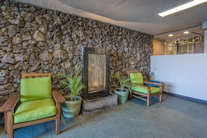 Un vestíbulo con paredes de piedra, un mostrador de recepción de madera y dos sillones verdes acolchados.