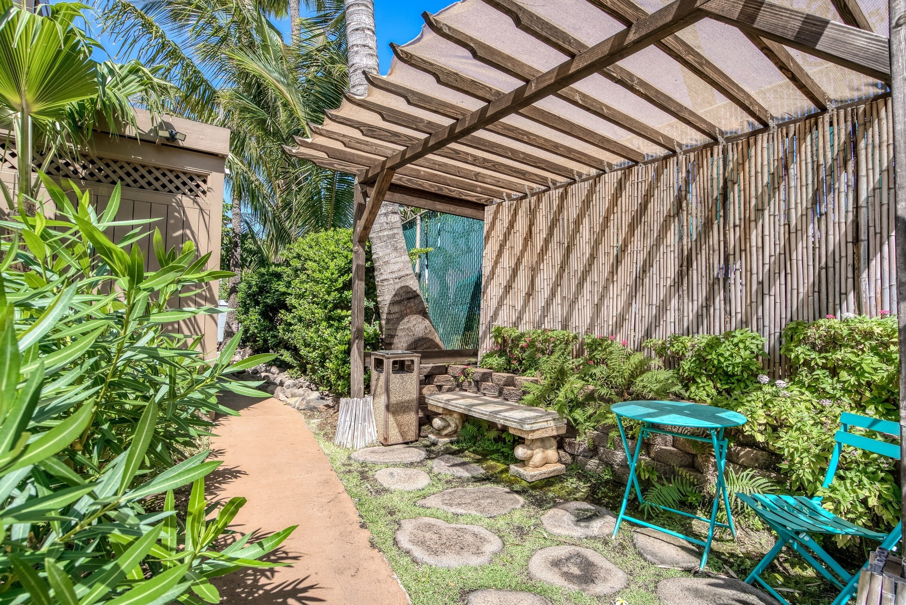 A covered patio area with a stone pathway, a stone bench, and a table with chairs.