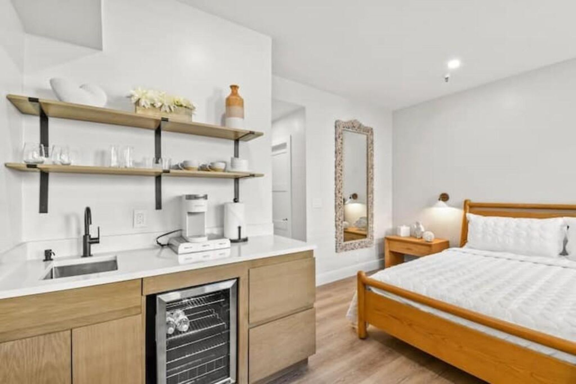 Habitación compacta con cama, mesita de noche y un mini refrigerador integrado.