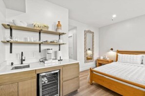 Une chambre à coucher de taille réduite, comprenant un lit, une table de chevet et un mini-réfrigérateur encastré.