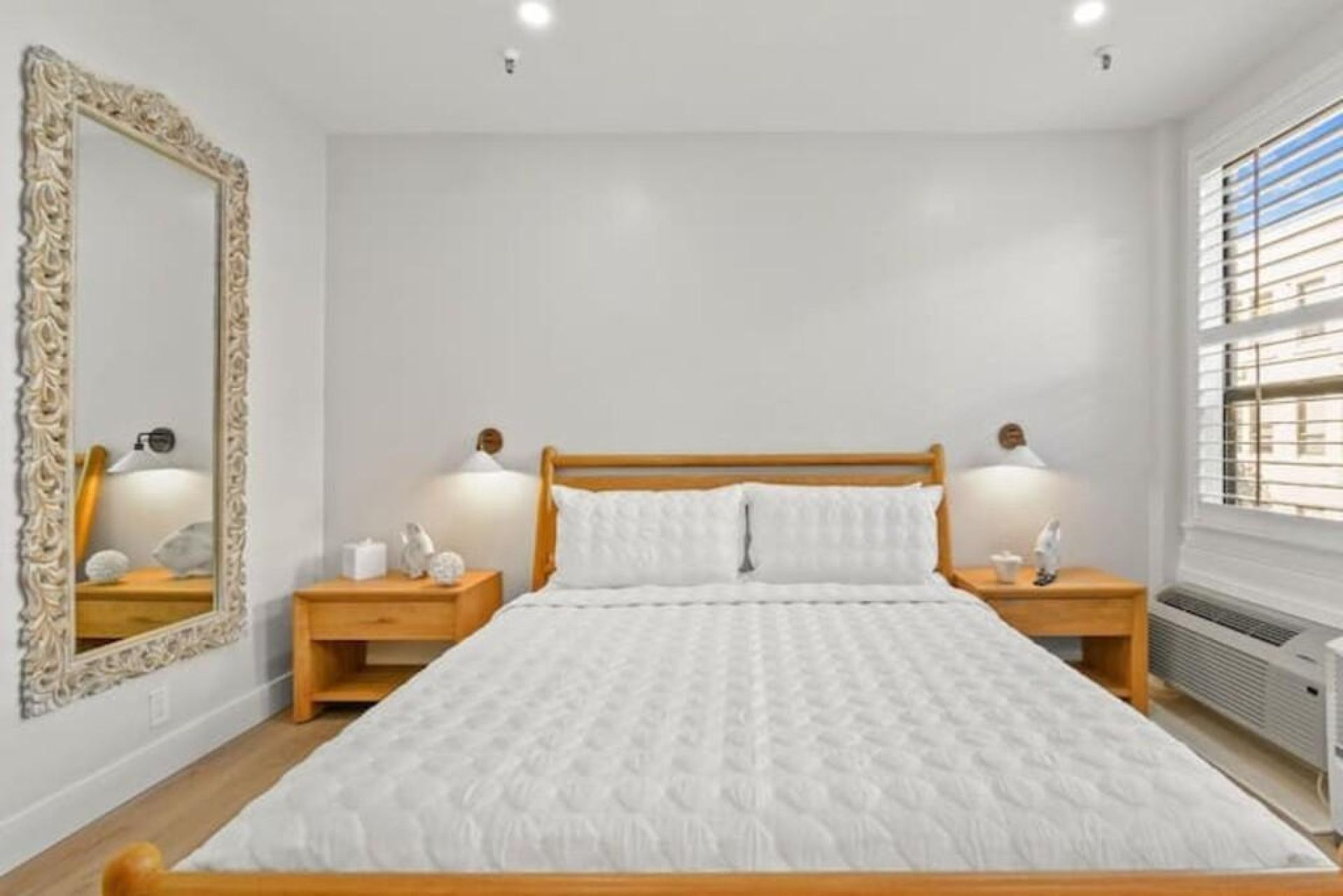 Une chambre à coucher avec un lit en bois, deux tables de chevet avec des lampes, un grand miroir et un radiateur.