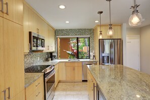 Una cocina moderna con armarios de madera, un refrigerador de acero inoxidable, horno empotrado e isla grande con encimera de granito.