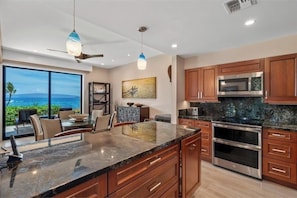 A modern kitchen with a large island, stainless steel appliances, and wooden cabinets. - Makena Surf, #g-101 2 Bedroom Condo by RedAwning (Kihei)