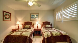A bedroom with two beds, a ceiling fan, a window with blinds, and artwork on the walls. - Kihei Beach, #402 2 Bedroom Condo by RedAwning (Kihei)