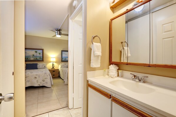 A hotel room with a bed, bedside table, lamp, and a bathroom with a sink, mirror, and towel rack.