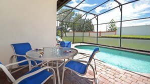 A covered patio area with a pool, blue chairs, and a table with drinks. - Happy Daze 4 Bedroom Home by RedAwning (Clermont)