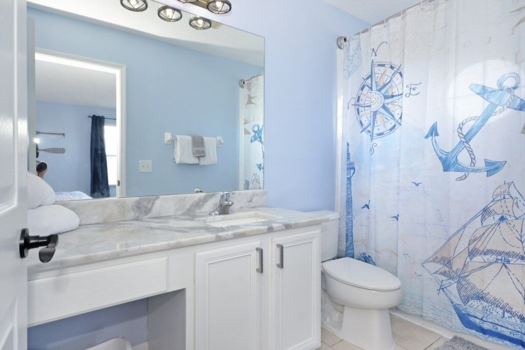Une salle de bain avec un lavabo en marbre, des toilettes blanches et un rideau de douche orné de motifs marins.