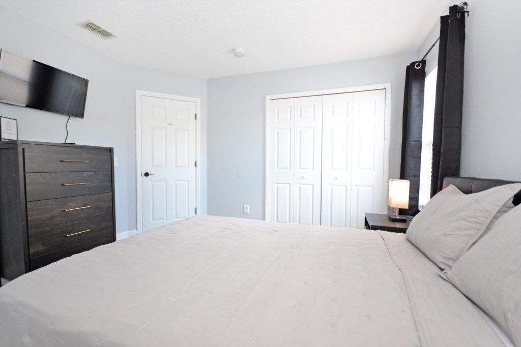 A bedroom with a bed, a dresser, a TV mounted on the wall, and two doors.