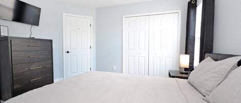 A bedroom with a bed, a dresser, a TV mounted on the wall, and two doors.