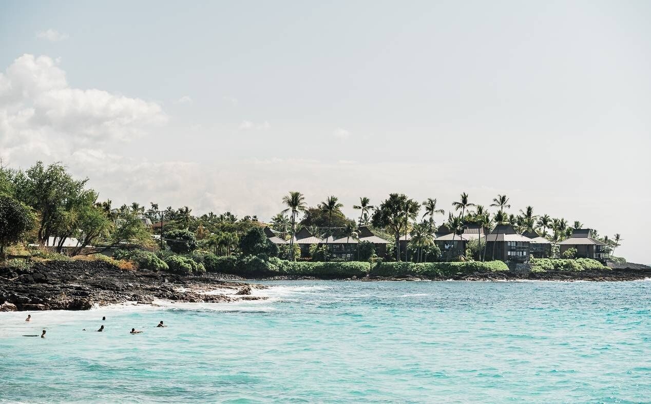 A beachfront hotel with multiple buildings, a rocky shoreline, and palm trees.