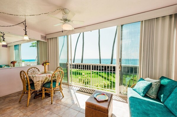 A room with a balcony overlooking the sea, furnished with a table, chairs, and a sofa. - Big Island Kona Magic Sands by Coldwell Banker Island Vacations (Kailua-Kona)