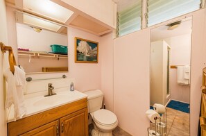 A bathroom with a white sink, wooden vanity, a toilet, and a shower area.