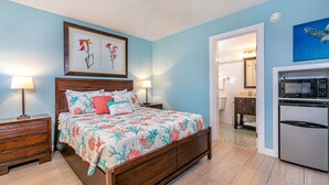 A bedroom with a bed, nightstands, a dresser, a bathroom with a toilet, sink, and mirror, and a kitchenette with a refrigerator and microwave. - Island Surf by Coldwell Banker Island Vacations (Kihei)