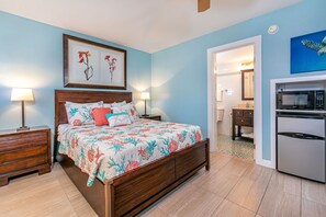 Une chambre comprenant un lit, des tables de chevet, une commode, une salle de bain avec des toilettes, un lavabo et un miroir, ainsi qu’une kitchenette équipée d’un réfrigérateur et d’un four à micro-ondes.