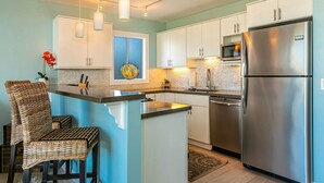 A modern kitchen with white cabinets, stainless steel appliances, and a central island. - Island Surf by Coldwell Banker Island Vacations (Kihei)