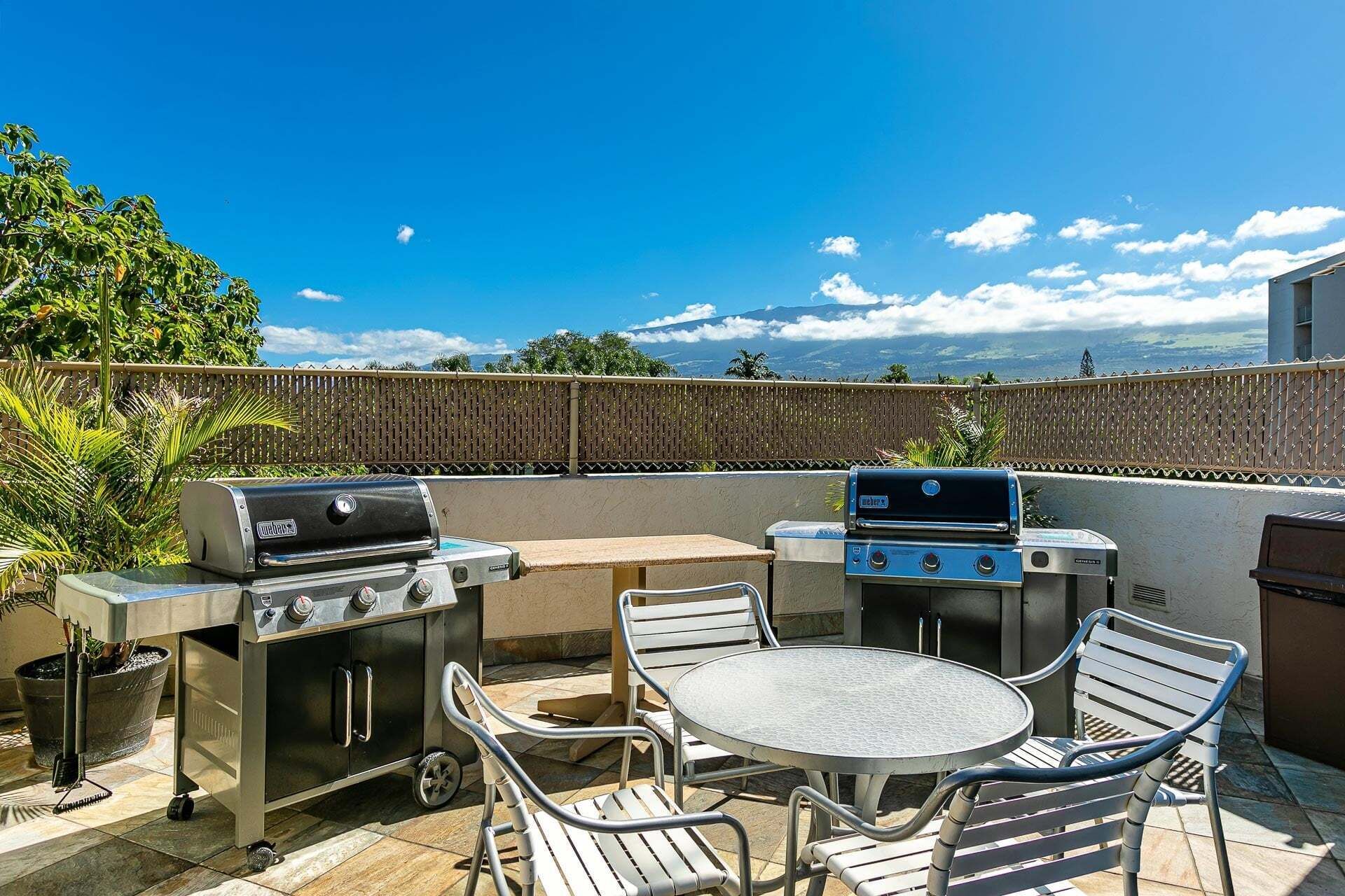 Eine Terrassengruppe mit zwei Grillplätzen, einem runden Metalltisch und vier Stühlen.