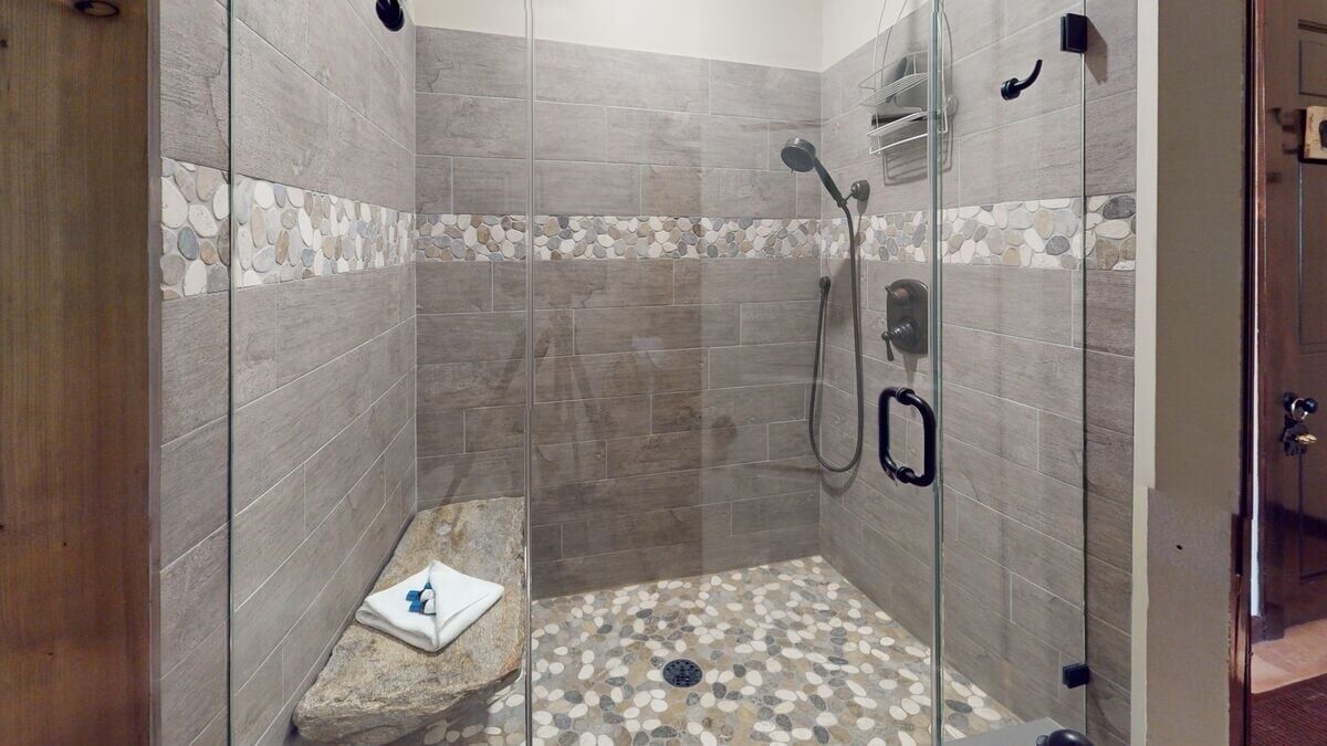 Une douche en verre avec un bord en mosaïque de pierre et une serviette posée sur un rocher.