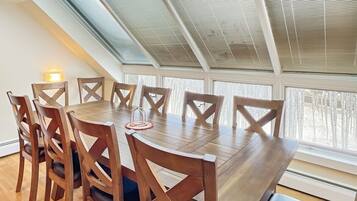 A dining area with a wooden table and chairs, large windows, and a skylight.