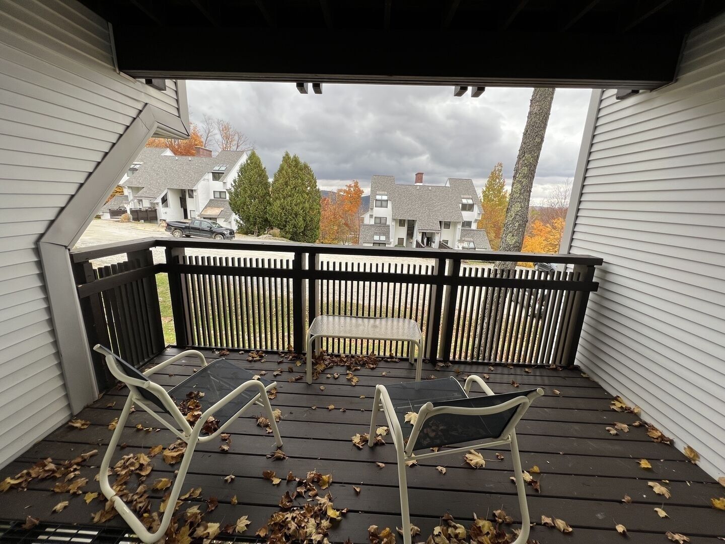 A covered outdoor area with a wooden deck, two white metal chairs, and a bench.