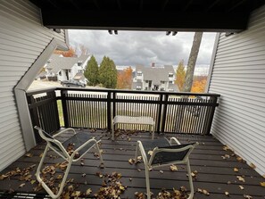A covered outdoor area with a wooden deck, two white metal chairs, and a bench.
