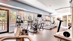 Un gimnasio con diversas máquinas de cardio, amplias ventanas y vistas al exterior.