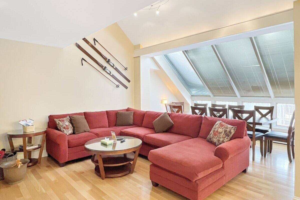 Un amplio salón con un sofá sectional rojo, una mesa de centro redonda y un comedor con sillas de madera y una mesa de vidrio.