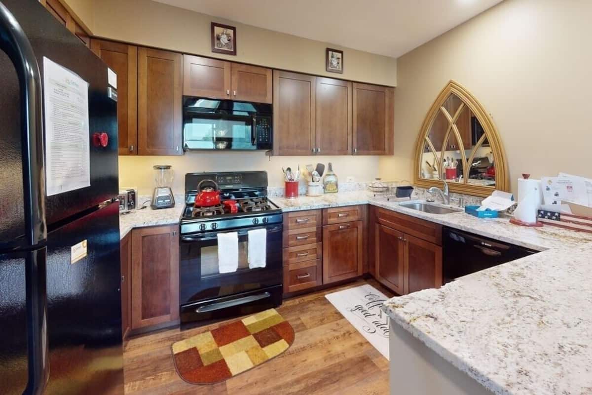 Una cocina con gabinetes de madera, un refrigerador negro, una estufa y un microondas.