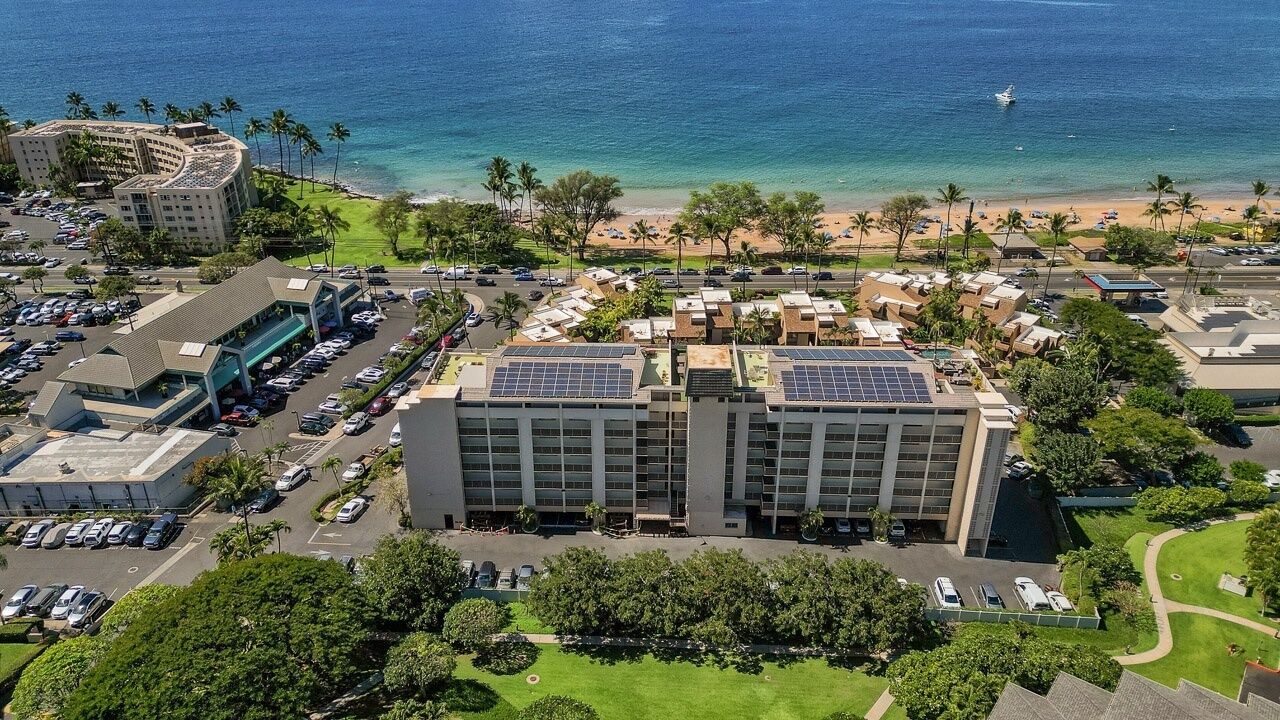 A hotel with a parking lot, a beach view, and solar panels on the roof.